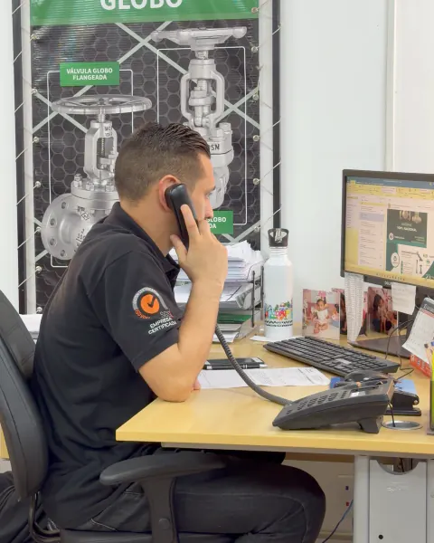 Atendente da BVI ao telefone, com o pôster da válvula globo ao fundo